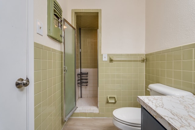 bathroom with vanity, toilet, tile walls, and a shower with shower door