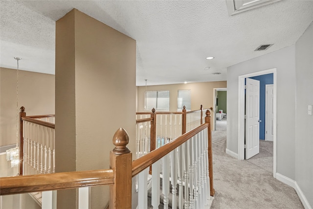 corridor with a textured ceiling and light colored carpet