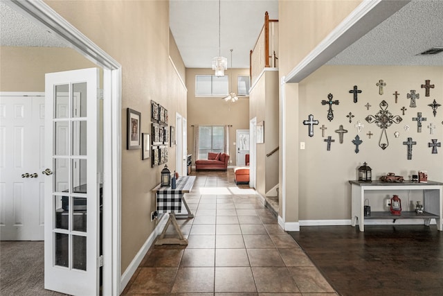 corridor featuring dark tile patterned floors, a chandelier, a textured ceiling, and a towering ceiling