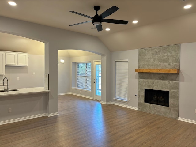 unfurnished living room with a tiled fireplace, dark wood-type flooring, vaulted ceiling, and ceiling fan