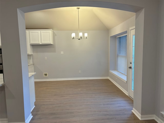 unfurnished dining area with lofted ceiling, light wood-type flooring, and an inviting chandelier