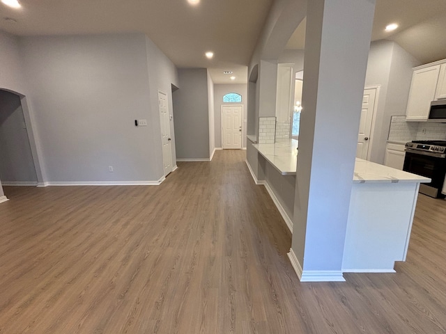 kitchen featuring tasteful backsplash, light stone countertops, appliances with stainless steel finishes, light wood-type flooring, and white cabinetry