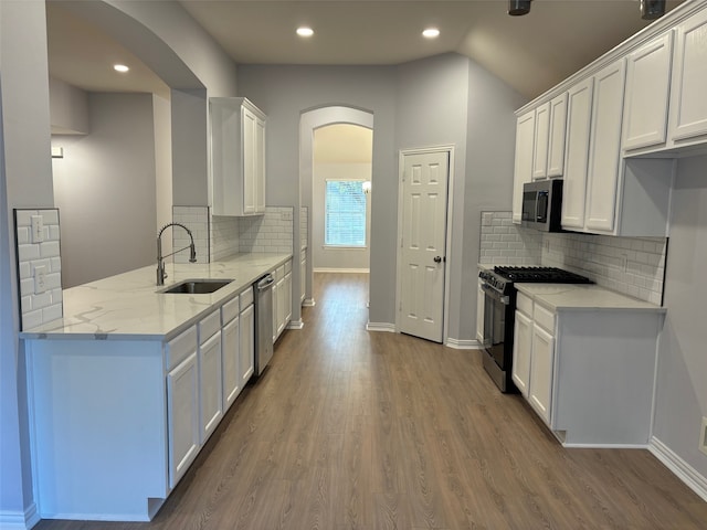 kitchen with appliances with stainless steel finishes, sink, white cabinets, light stone counters, and hardwood / wood-style flooring