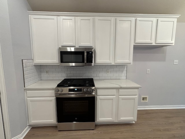 kitchen featuring light stone countertops, stainless steel appliances, tasteful backsplash, and white cabinets