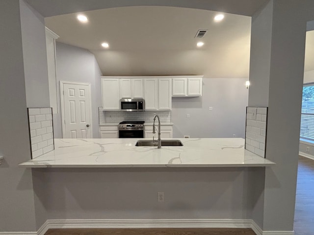 kitchen featuring kitchen peninsula, white cabinets, light stone counters, appliances with stainless steel finishes, and sink