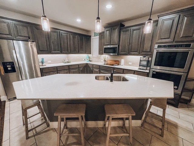 kitchen featuring stainless steel appliances, an island with sink, hanging light fixtures, and sink