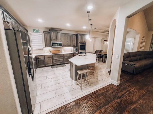 kitchen featuring a breakfast bar, pendant lighting, an island with sink, dark brown cabinetry, and stainless steel appliances