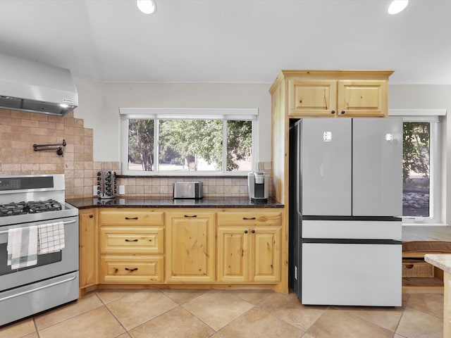 kitchen with dark stone countertops, wall chimney range hood, stainless steel range, and white refrigerator