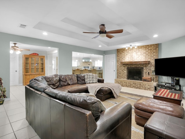 tiled living room with ceiling fan, a fireplace, and a raised ceiling