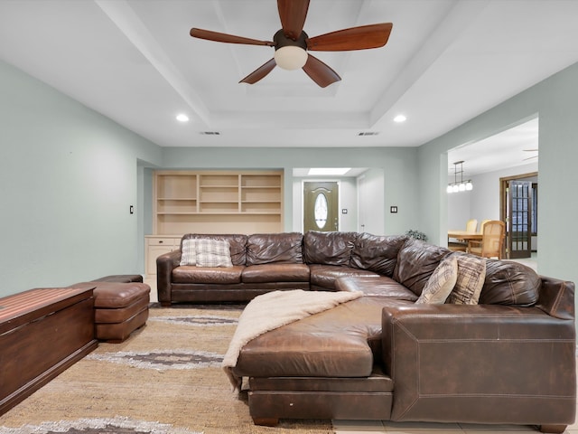 living room with a healthy amount of sunlight, ceiling fan with notable chandelier, and a raised ceiling