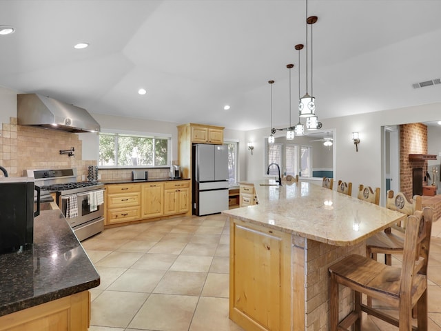 kitchen featuring a spacious island, gas stove, hanging light fixtures, wall chimney exhaust hood, and white fridge