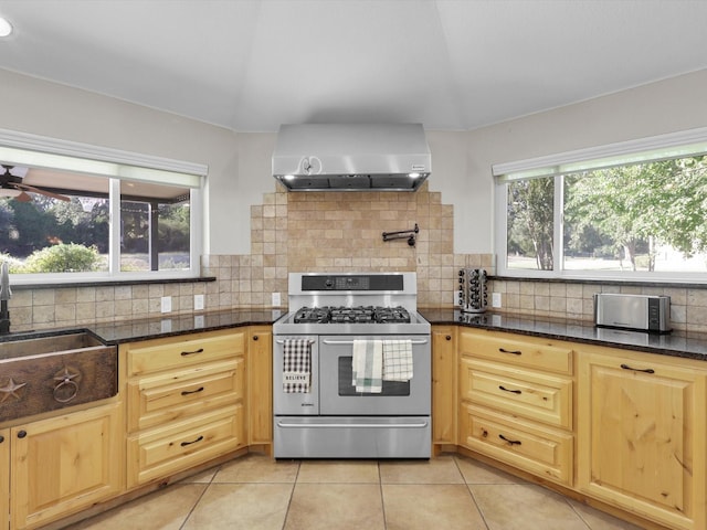 kitchen with wall chimney range hood, decorative backsplash, a sink, range with two ovens, and light tile patterned flooring