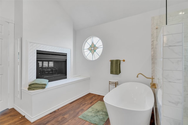 bathroom with a multi sided fireplace, a tub, hardwood / wood-style floors, and lofted ceiling