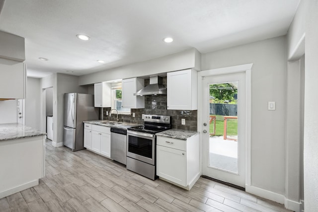 kitchen with light stone counters, appliances with stainless steel finishes, wall chimney range hood, and white cabinets