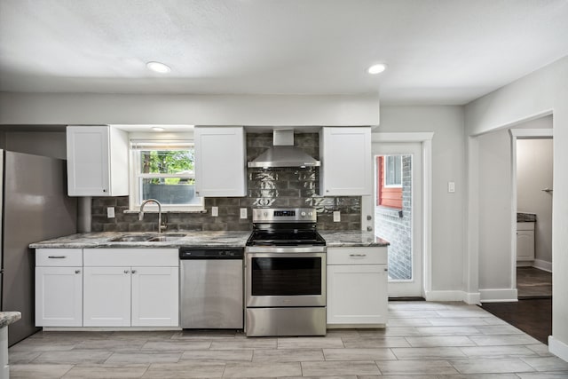 kitchen featuring appliances with stainless steel finishes, wall chimney exhaust hood, white cabinetry, and sink