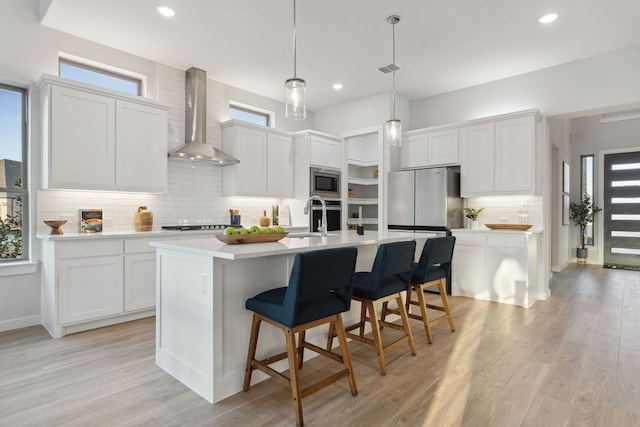 kitchen with white cabinetry, wall chimney range hood, appliances with stainless steel finishes, and plenty of natural light