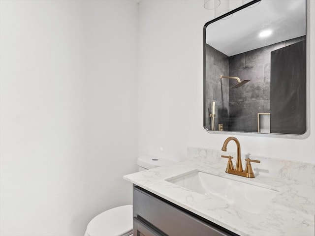 bathroom featuring toilet, tiled shower, and vanity