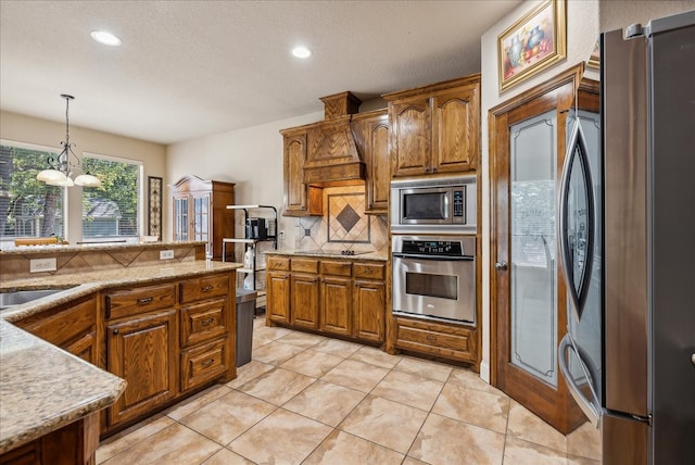 kitchen featuring backsplash, appliances with stainless steel finishes, pendant lighting, light tile patterned floors, and premium range hood