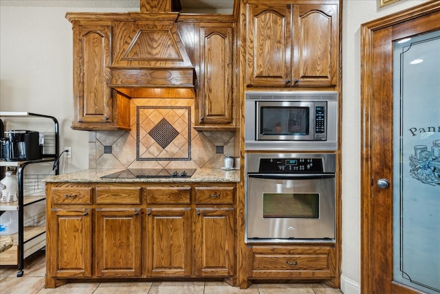 kitchen featuring appliances with stainless steel finishes, light stone counters, light tile patterned flooring, and tasteful backsplash