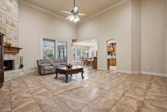 living room featuring a towering ceiling, ceiling fan, a stone fireplace, and ornamental molding