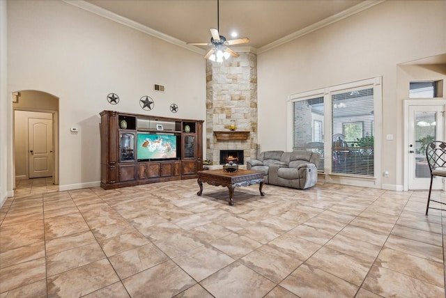 living room with crown molding, a stone fireplace, a towering ceiling, and ceiling fan