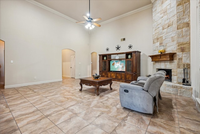 living room featuring a towering ceiling, crown molding, a fireplace, and ceiling fan