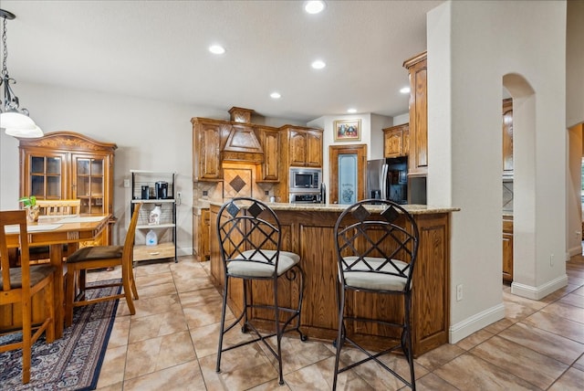 kitchen featuring appliances with stainless steel finishes, backsplash, kitchen peninsula, light stone counters, and a breakfast bar