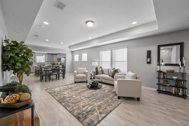 living room with light wood-type flooring and a raised ceiling