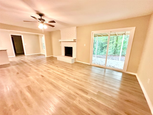 unfurnished living room featuring a brick fireplace, light wood-type flooring, and ceiling fan