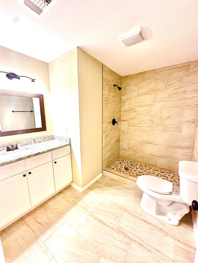 bathroom featuring vanity, a textured ceiling, toilet, and a tile shower