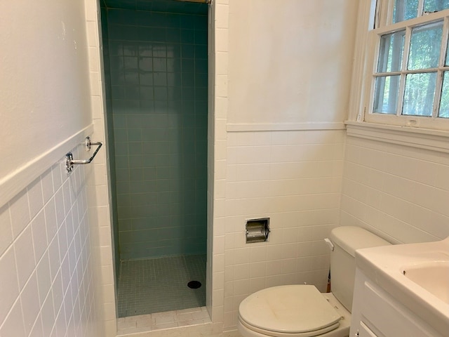 bathroom with toilet, vanity, tile walls, and tiled shower