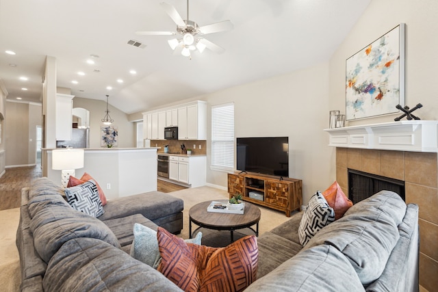 living room with ceiling fan, lofted ceiling, and a tile fireplace