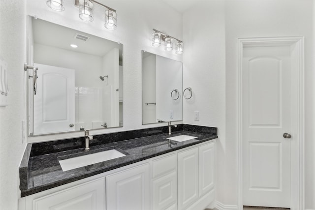 bathroom featuring double vanity, visible vents, walk in shower, and a sink