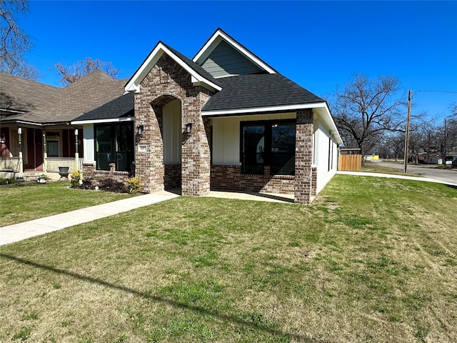 view of front of home featuring brick siding, a porch, a shingled roof, and a front yard