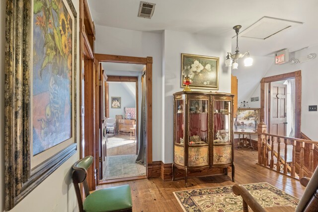 corridor featuring a notable chandelier, hardwood / wood-style flooring, and vaulted ceiling