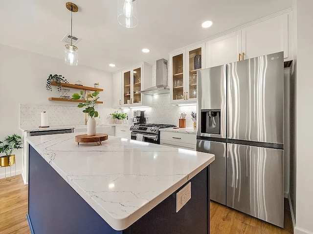 kitchen featuring appliances with stainless steel finishes, wall chimney exhaust hood, light hardwood / wood-style flooring, white cabinets, and hanging light fixtures