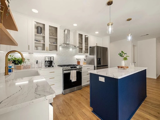 kitchen featuring sink, wall chimney exhaust hood, light stone counters, light hardwood / wood-style flooring, and appliances with stainless steel finishes