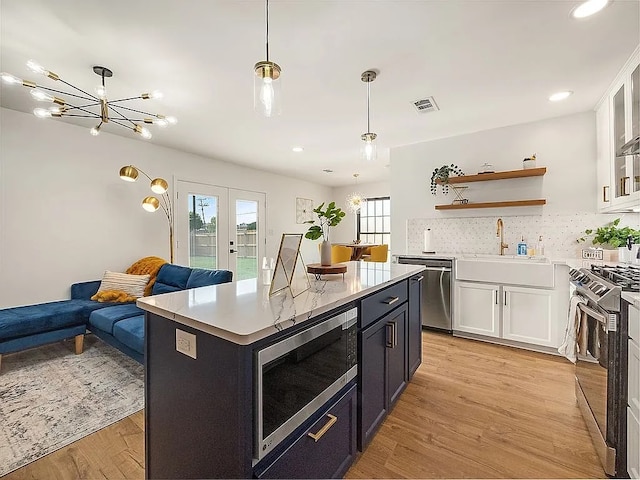 kitchen featuring appliances with stainless steel finishes, pendant lighting, white cabinets, light hardwood / wood-style floors, and a kitchen island