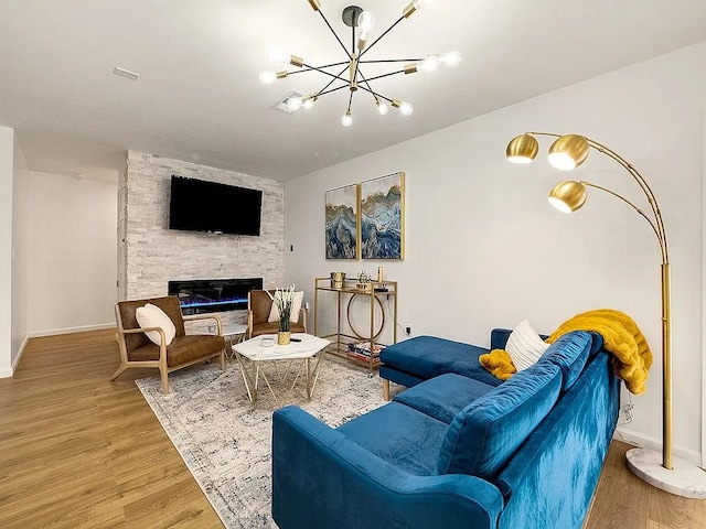 living room featuring a stone fireplace, wood-type flooring, and an inviting chandelier