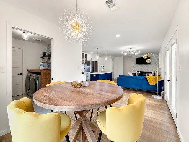 dining space with a fireplace, light hardwood / wood-style flooring, and a notable chandelier