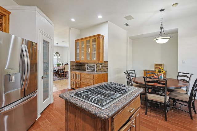 kitchen featuring decorative backsplash, appliances with stainless steel finishes, pendant lighting, light hardwood / wood-style flooring, and a kitchen island