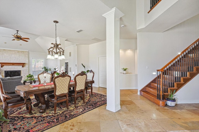 dining area with ceiling fan with notable chandelier, a stone fireplace, ornate columns, and high vaulted ceiling