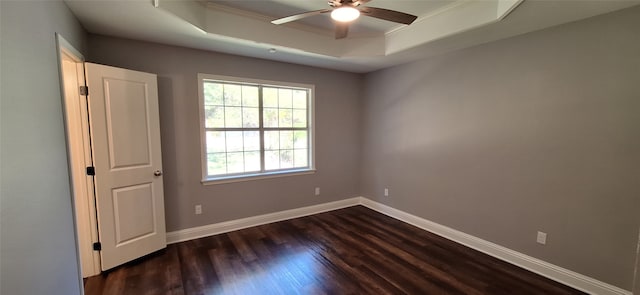 empty room with ornamental molding, ceiling fan, a tray ceiling, and dark hardwood / wood-style flooring