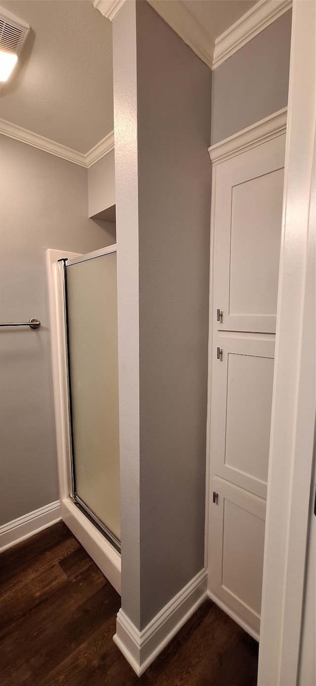 bathroom with ornamental molding, a shower with shower door, and hardwood / wood-style floors