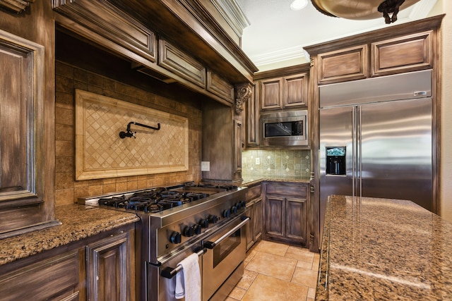 kitchen with built in appliances, dark brown cabinets, dark stone counters, ornamental molding, and tasteful backsplash