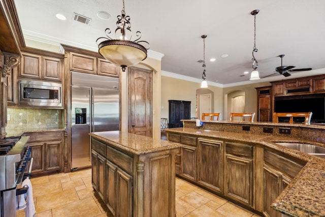 kitchen with decorative backsplash, built in appliances, hanging light fixtures, sink, and a center island