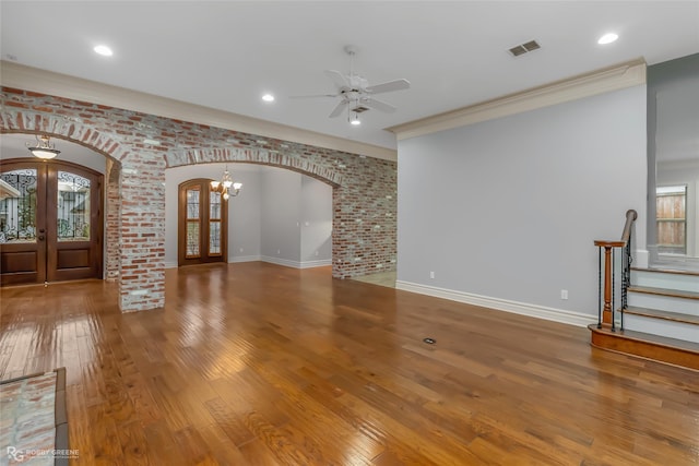 unfurnished living room with french doors, crown molding, hardwood / wood-style flooring, ceiling fan, and brick wall