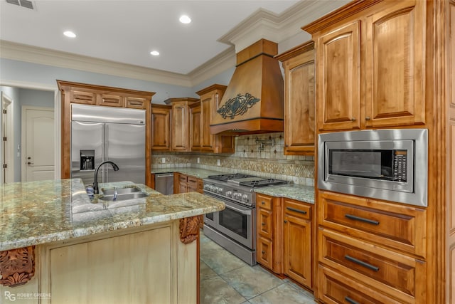 kitchen featuring sink, built in appliances, tasteful backsplash, an island with sink, and custom exhaust hood