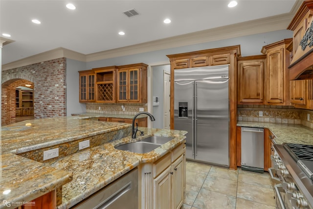 kitchen with sink, premium appliances, ornamental molding, light stone countertops, and decorative backsplash