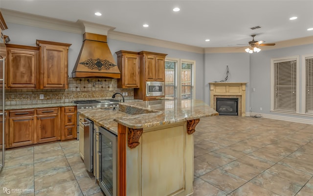 kitchen featuring appliances with stainless steel finishes, wine cooler, custom exhaust hood, light stone counters, and a center island with sink